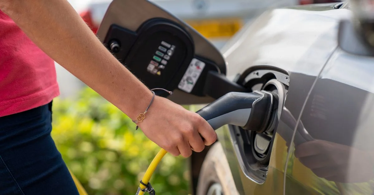Gros plan sur une personne branchant sa voiture électrique à une borne de recharge extérieure.