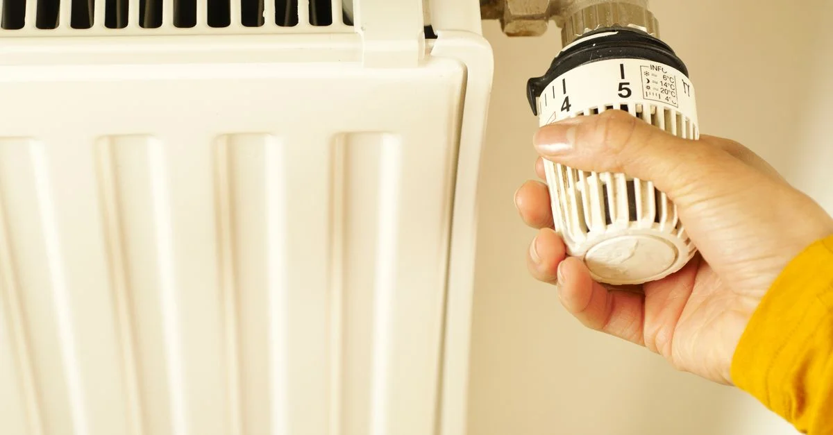 Gros plan de la main ajustant le thermostat du radiateur pour contrôler la température de chauffage dans la maison.