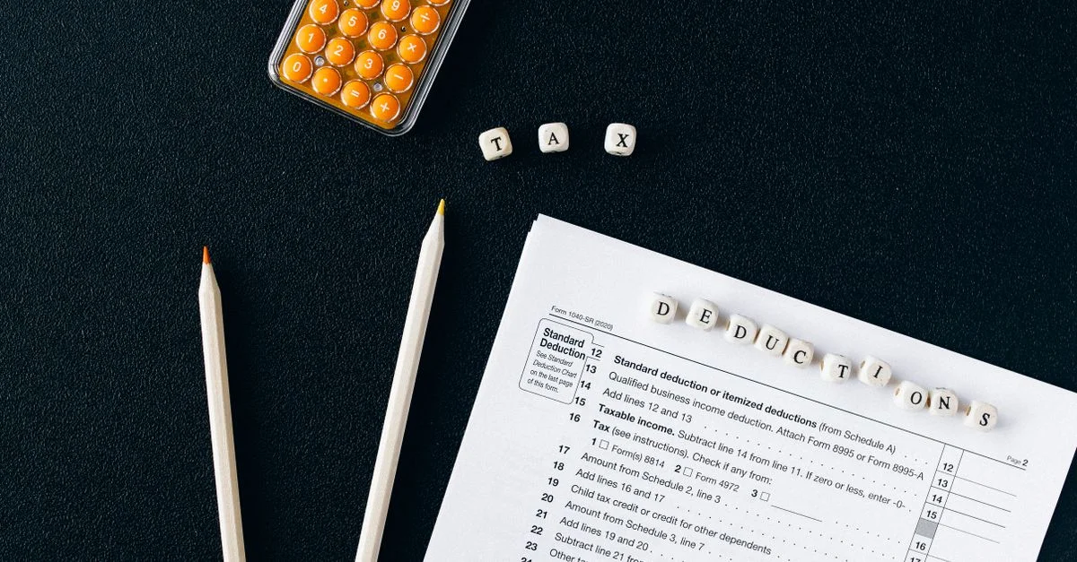 Vue de dessus d'un formulaire fiscal, de crayons et d'une calculatrice sur un fond noir, mettant en avant les déductions fiscales.