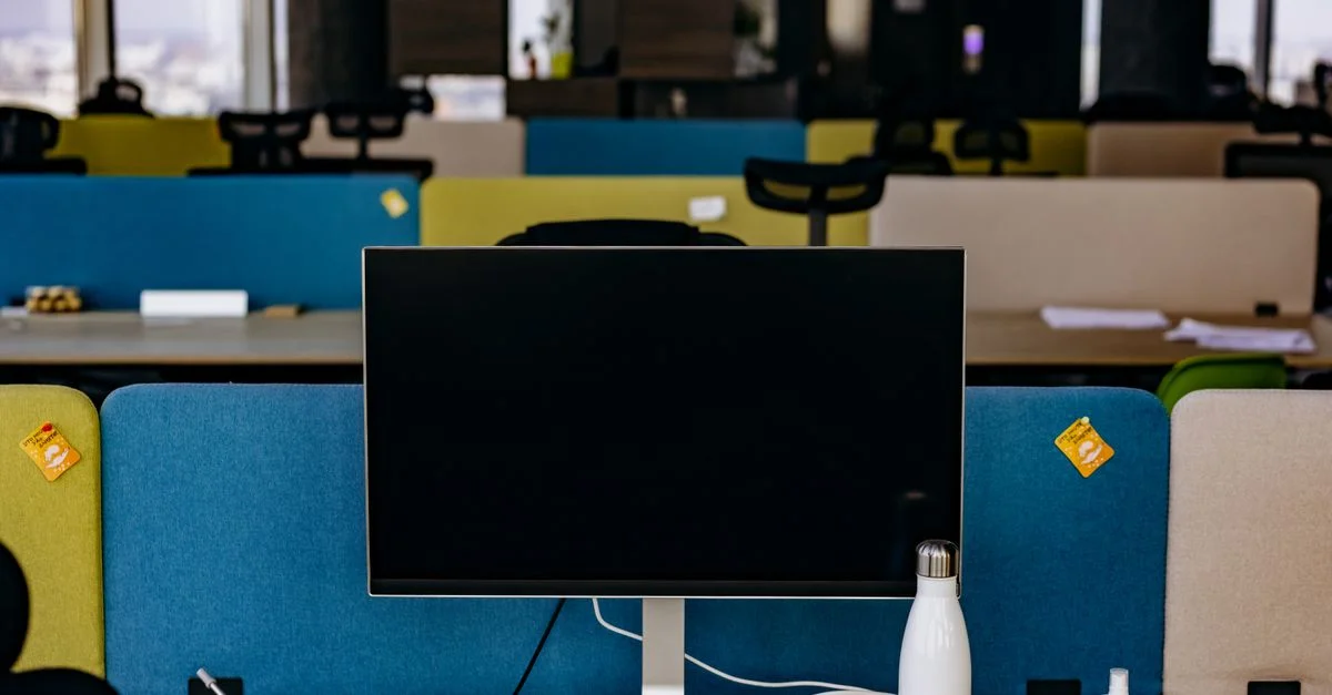 Une configuration de bureau contemporaine avec un moniteur, des cloisons et des accessoires sur un bureau dans un bureau open space.