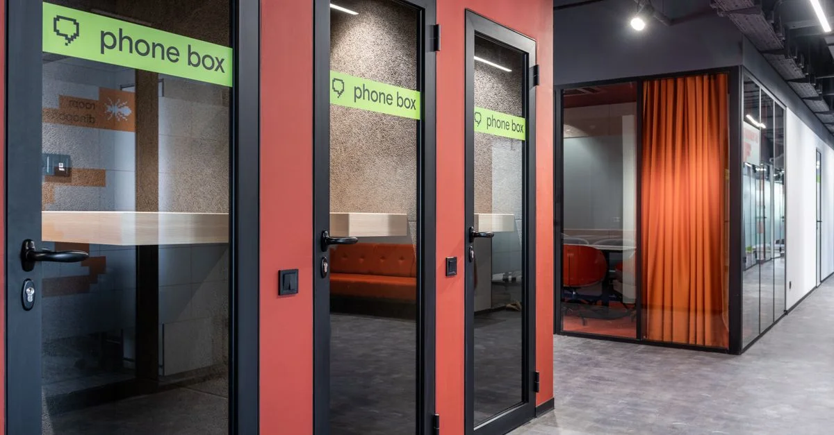 Couloir de bureau élégant avec des cabines téléphoniques en verre modernes et un design intérieur vibrant.